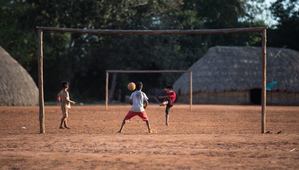 Crianças jogando futebol. Foto captada durante a festa de comemoração dos 10 anos do Movimento das Mulheres Yarang (MMY). O MMY produz e coleta sementes nativas para o reflorestamento das nascentes e matas ciliares da bacia do rio Xingu no entorno do TIX, Aldeia Moygu, Mato Grosso @Carol Quintanilha / ISA