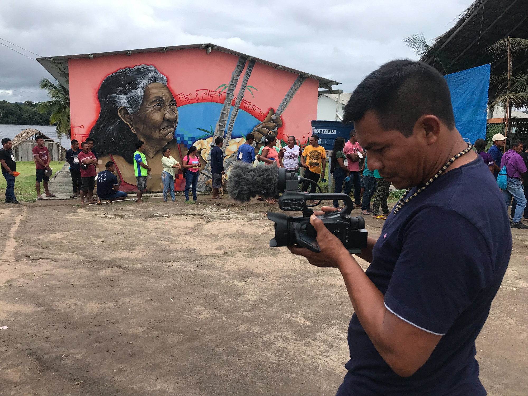 Comunicador da Rede Wayuri, Moisés Baniwa filma o encontro. Ao fundo, mural da indígena Mirtes Sanches, do povo Baré, a moradora mais antiga de Cartucho 📷 Ana Amélia Hamdan/ISA