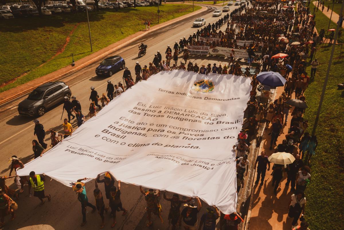 Participantes do Acampamento Terra Livre de 2026, carregam faixa que representa o documento de demarcação de terras a ser assinado pelo presidente e pelo Ministro da Justiça, em Brasília